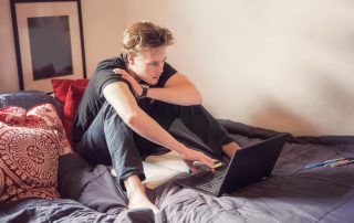 male sitting on his bed on his laptop