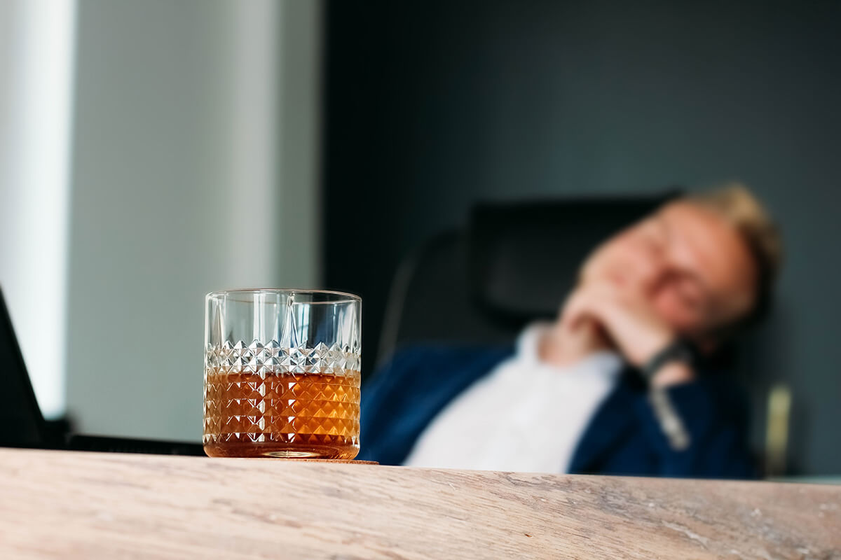 man with drink at desk wondering Is Alcohol a Drug