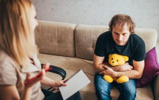 man on couch with teddybear dealing with childhood trauma - Mental Health treatment