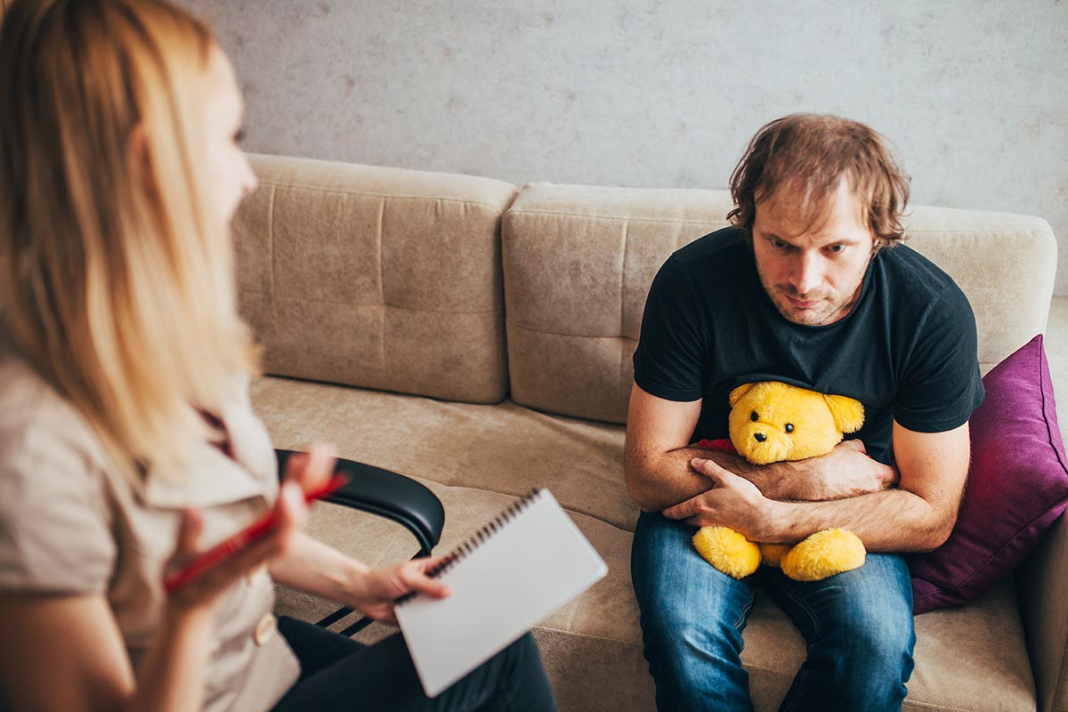 man on couch with teddybear dealing with childhood trauma - Mental Health treatment