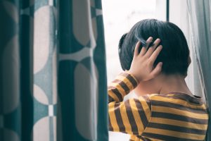 Little Asian boy wear long sleeve stripe shirt stand by window, hand cover ears, crying and screaming. Feeling frustration, anxiety, fear, stressed. Childhood Trauma and mental illness concept.