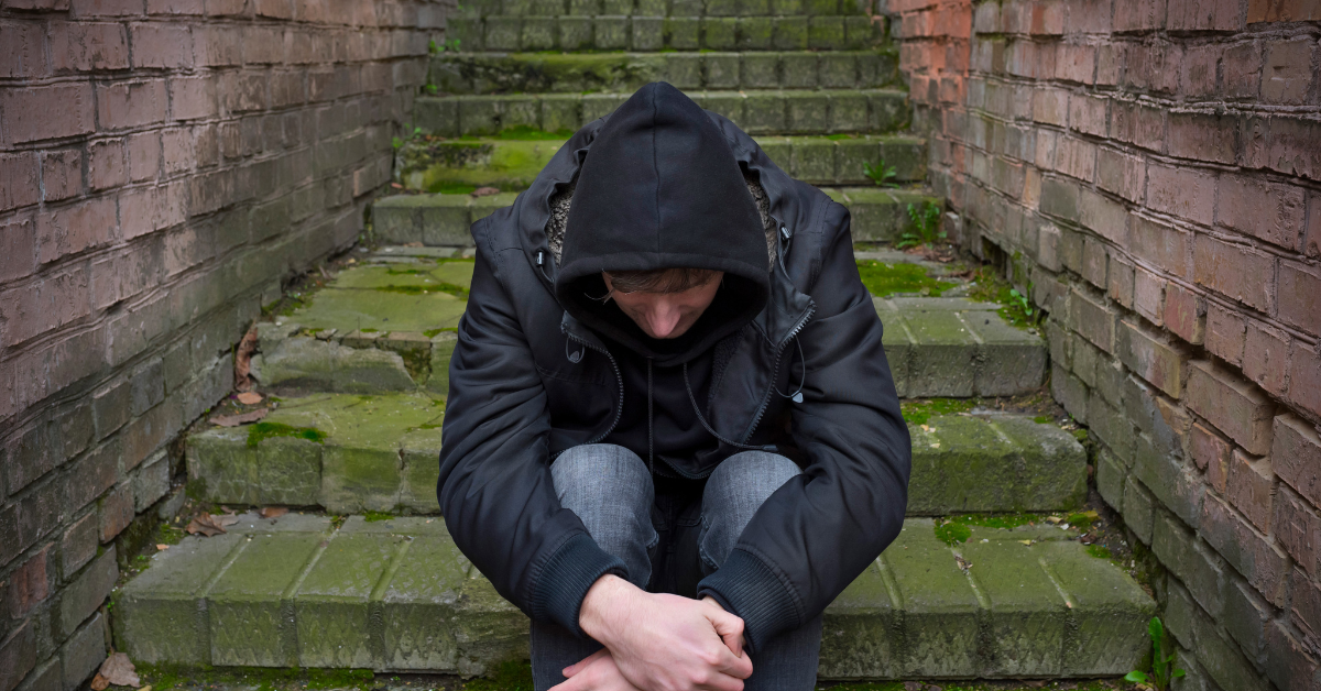A man sits with his hood on in the center of some steps.