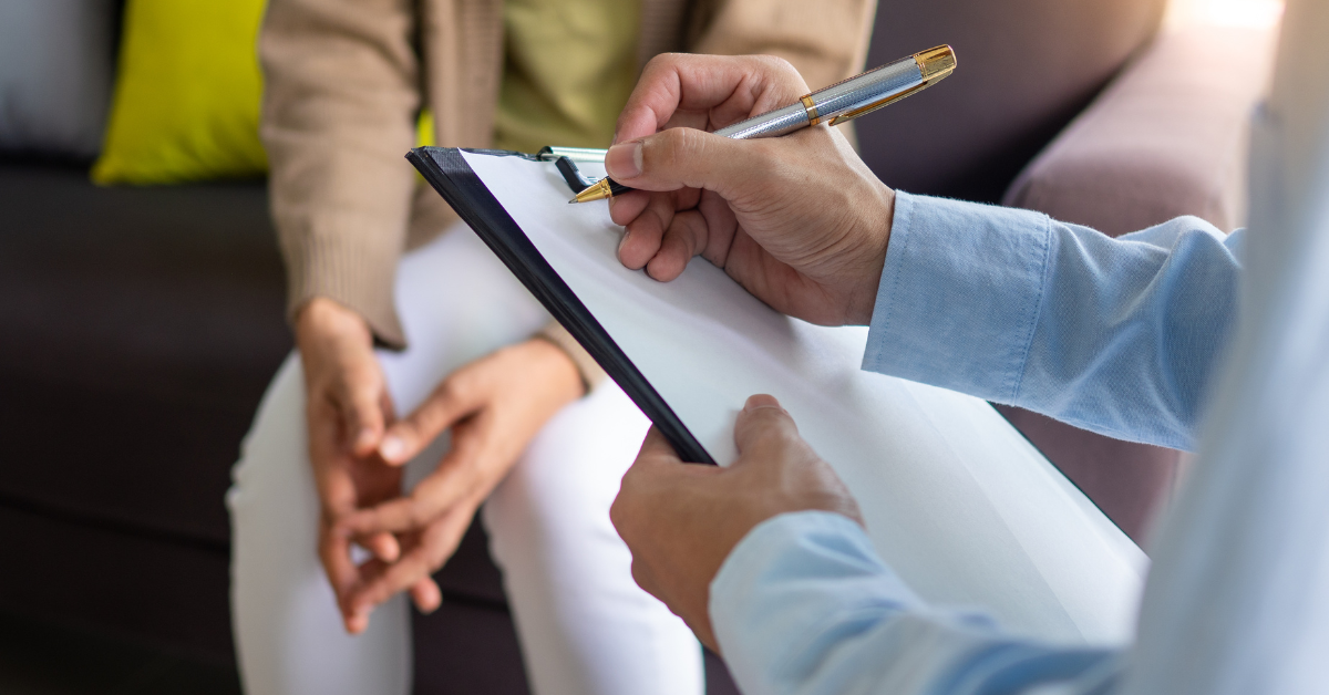 A set of hands writes on a clipboard facing another set of hands.