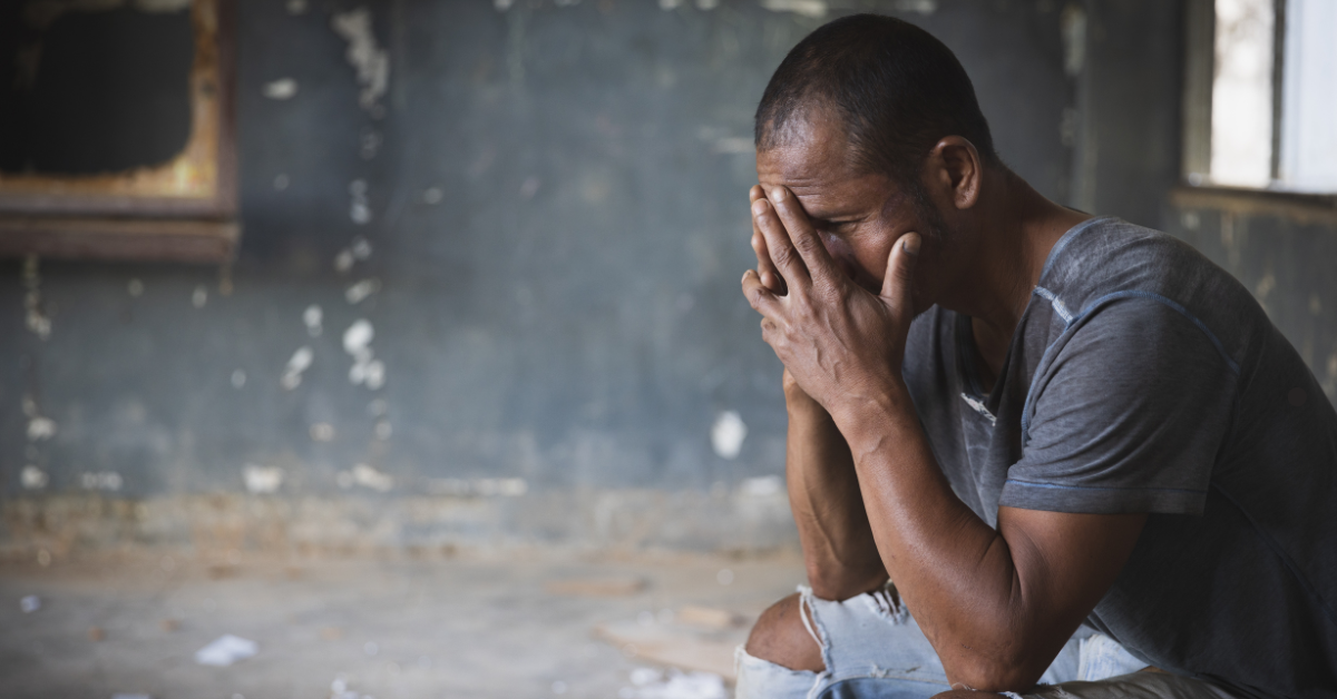 A man sits in a dilapidated room with his head in his hands.