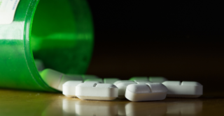 A green pill bottle tipped on its side, with white oblong pills spilling out onto a dark surface.
