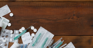 A wooden surface with various drug paraphernalia scattered across it. This includes syringes, pill bottles, and blister packs of pills.