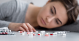 A woman lays her head down staring at several types of pills and capsules.