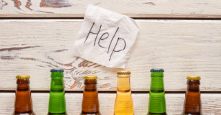 A napkin with the word "help" written on it, next to three bottles of beer on a wooden table.