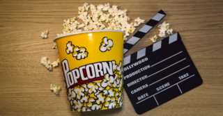 A bucket of popcorn sitting on a wooden table next to a clapperboard. The clapperboard has text on it that says "Hollywood Production" "Director" "Camera" "Date" "Scene" "Take".