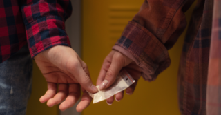 Hand of one person passes a small baggie to another.