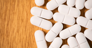 A pile of white pills on a wooden table.