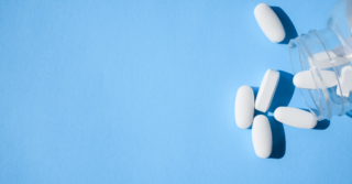 White pills spilling out of a clear jar onto a blue background.