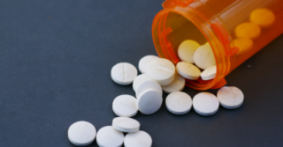 A pile of white pills spilling out of an orange prescription bottle onto a dark surface.
