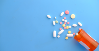 A pile of colorful pills spilling out of an orange prescription bottle onto a blue background.