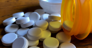 A pile of white pills spilling out of an orange prescription bottle onto a wooden surface.